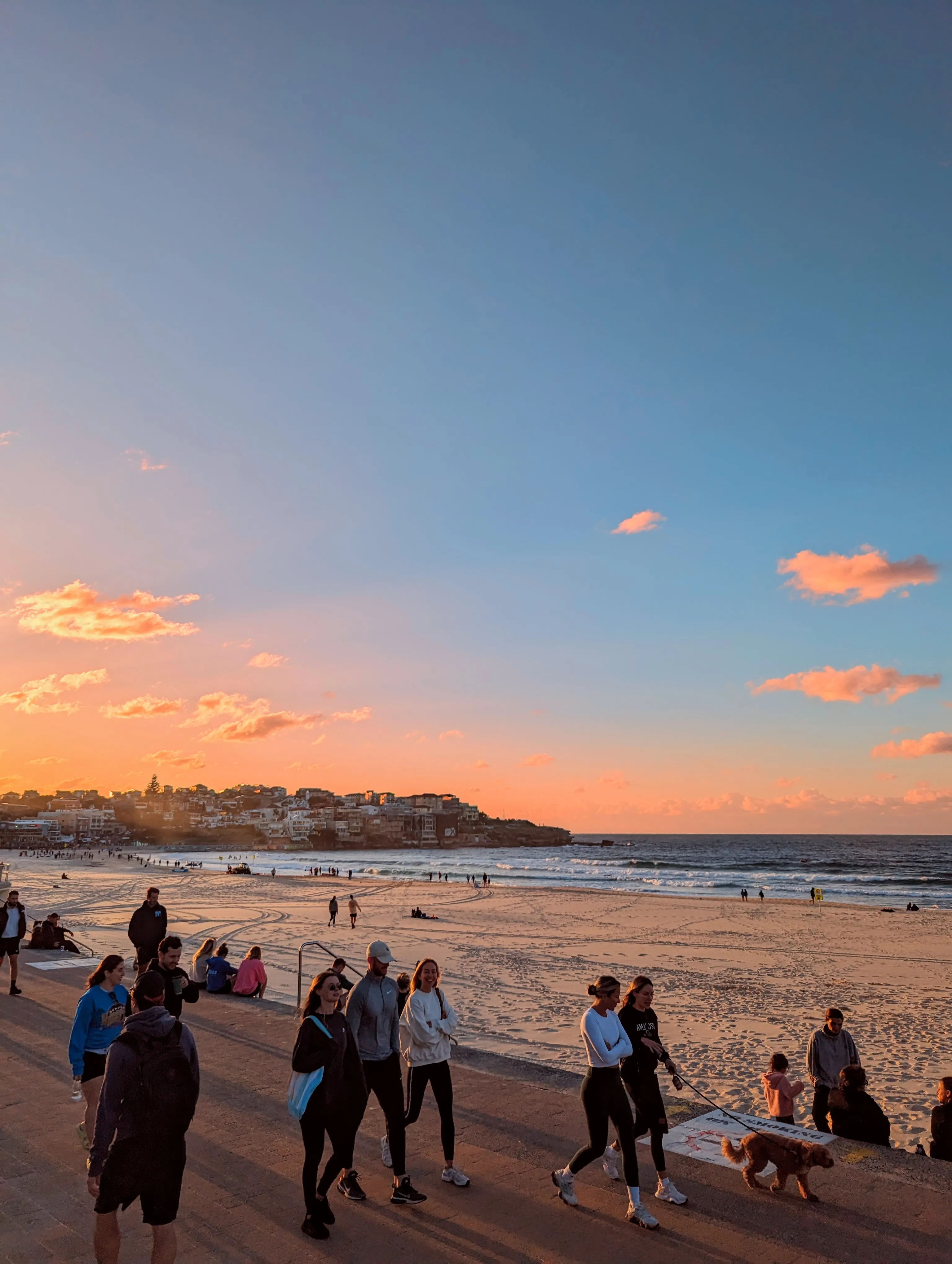 Sunset over Bondi Beach, with people walking along the promenade